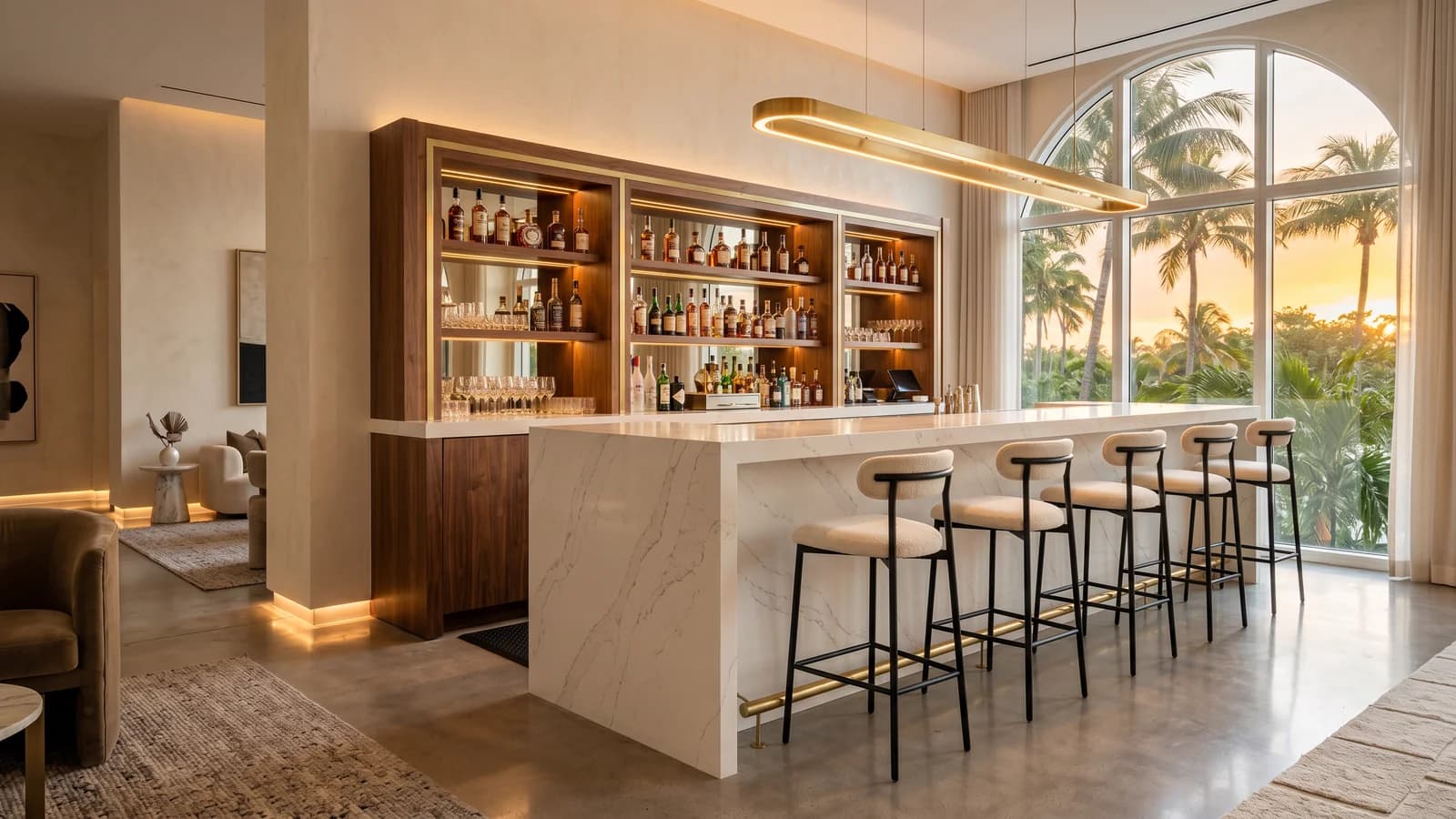 Luxury boutique hotel lobby bar in Miami Beach with full-height polished Spanish white quartz countertop and waterfall front, walnut back-bar shelving with brushed brass, matte black bar stools, statement brass pendant