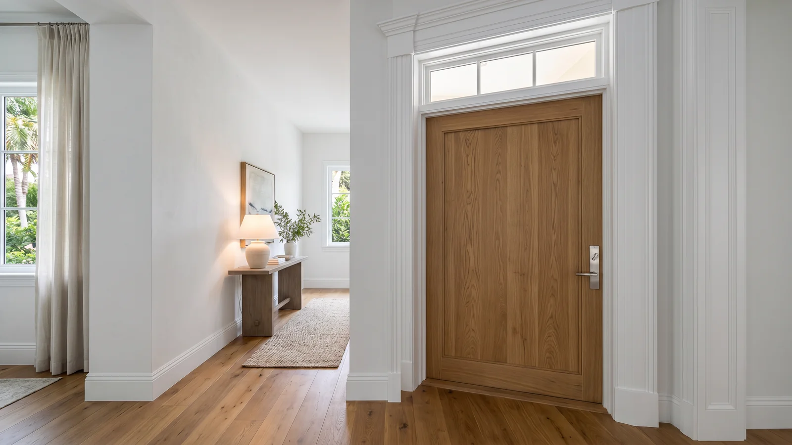 Entrada del dormitorio principal en residencia de lujo en Coral Gables con puerta de roble blanco macizo sobredimensionada, herraje de níquel cepillado, moldura blanca, piso engineered tablón ancho, luz suave de mañana por el transom