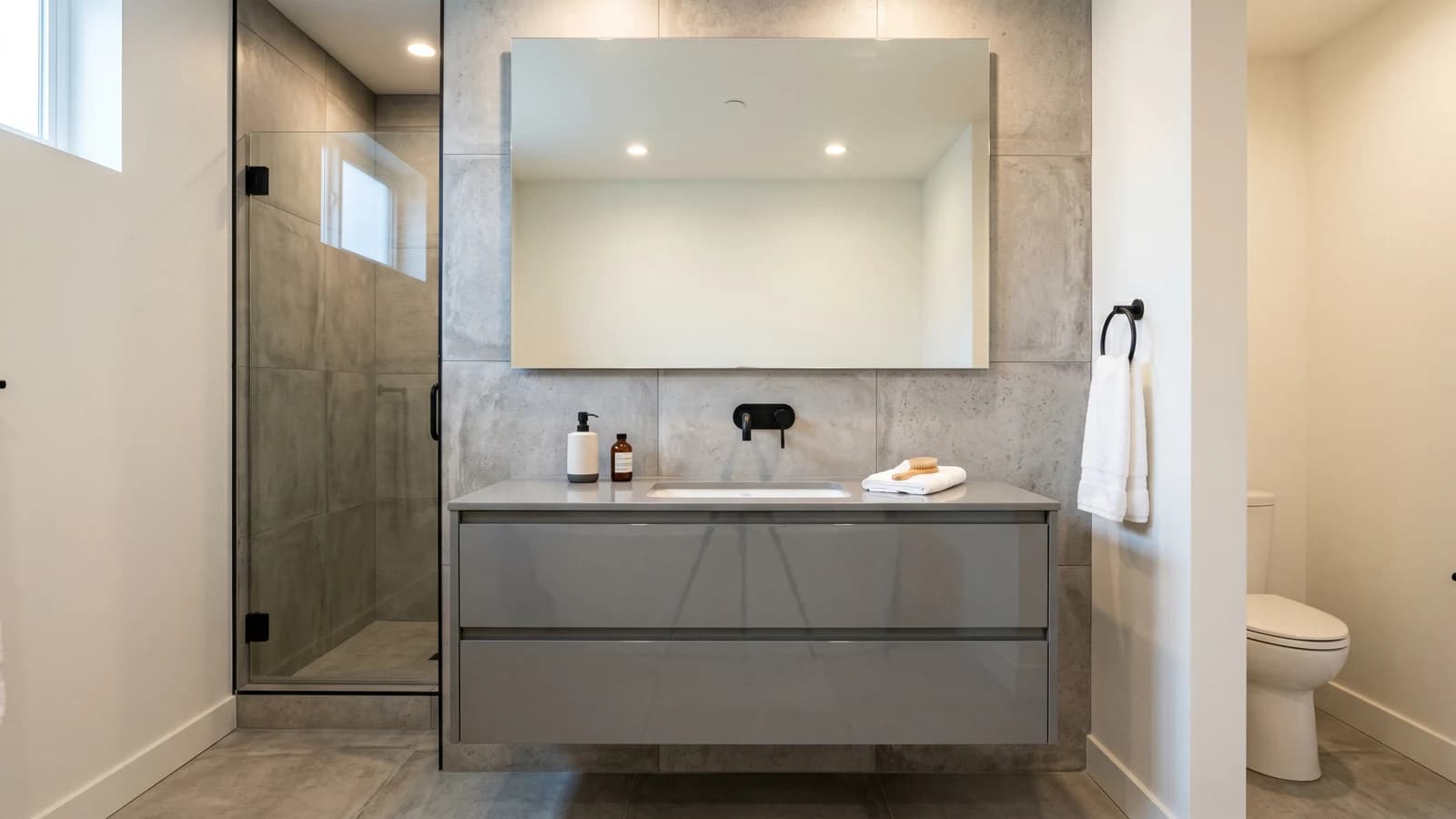 Modern multifamily model unit bathroom in Doral with a 48-inch floating gray lacquer vanity, two integrated drawers, undermount rectangular sink, matte black wall-mounted faucet, large-format concrete-look porcelain, recessed ceiling lighting