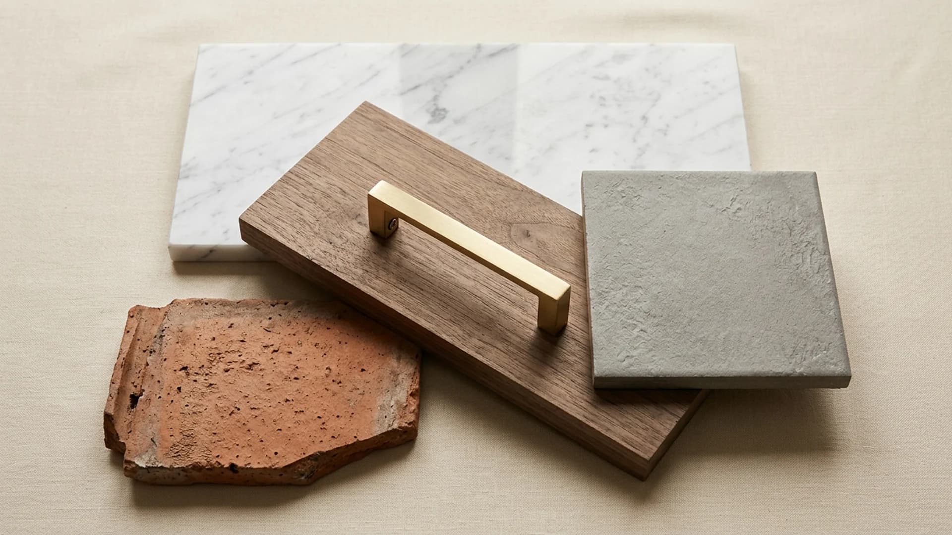 Bodegón multi-material — porcelanato, walnut con tirador de bronce cepillado, concreto y terracota sobre lino crema